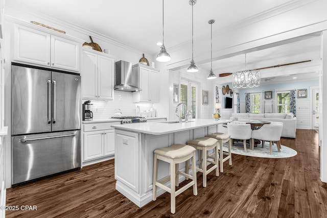 kitchen featuring high end refrigerator, wall chimney range hood, a sink, white cabinetry, and dark wood-type flooring