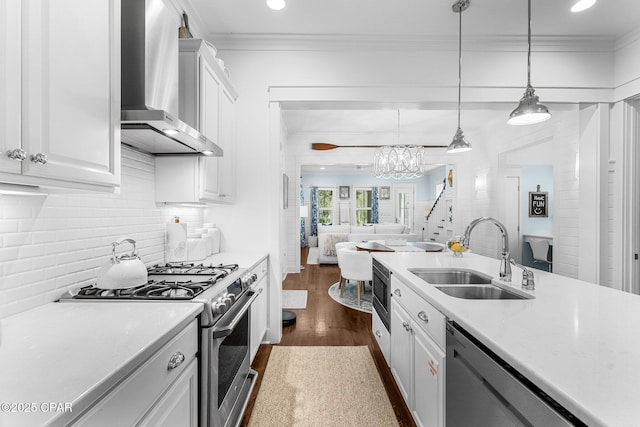 kitchen featuring ornamental molding, a sink, wall chimney exhaust hood, appliances with stainless steel finishes, and open floor plan
