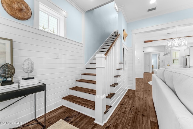 staircase featuring wood finished floors, visible vents, crown molding, and a notable chandelier