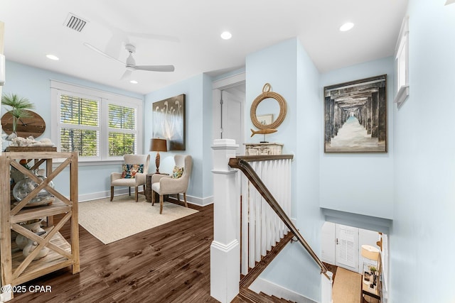 living area featuring a ceiling fan, an upstairs landing, visible vents, baseboards, and dark wood-style floors