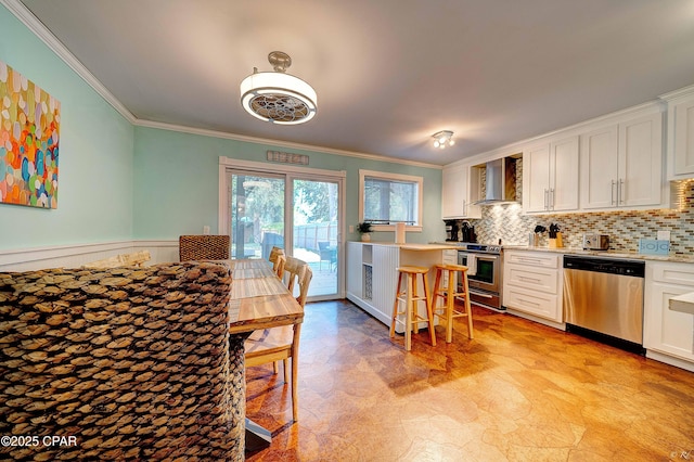 kitchen with stainless steel appliances, crown molding, wall chimney range hood, light countertops, and white cabinets