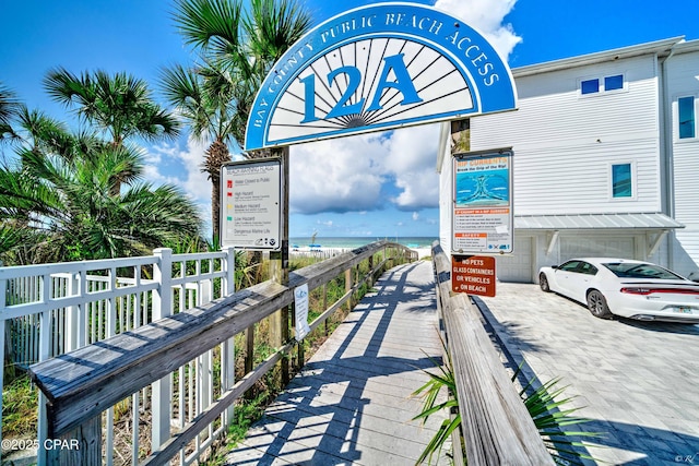 view of community with driveway, a garage, and view of water and beach