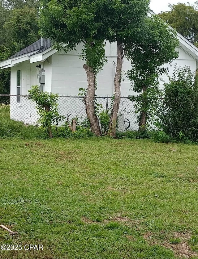 view of side of property with fence, a lawn, and a shingled roof