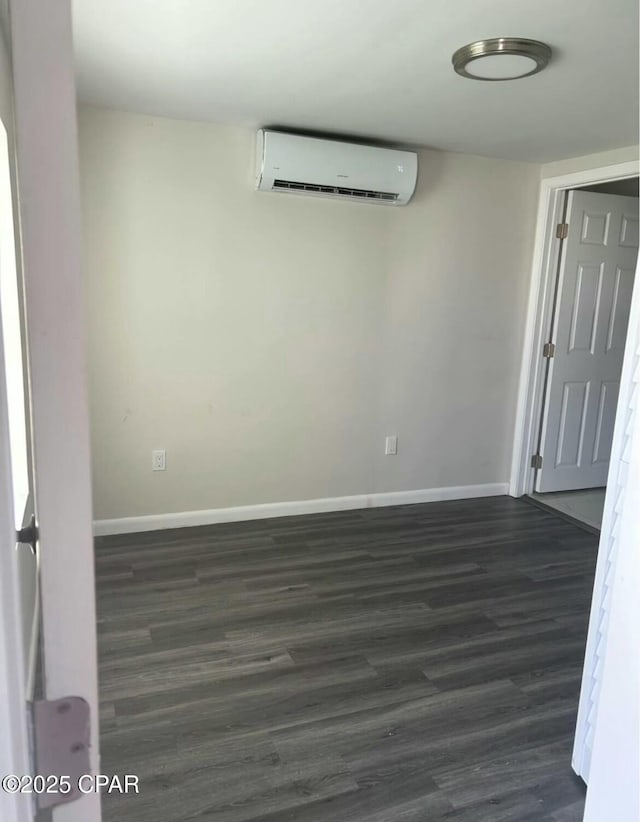 unfurnished room with baseboards, an AC wall unit, and dark wood-type flooring