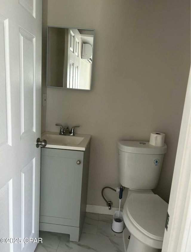 half bathroom featuring baseboards, marble finish floor, vanity, and toilet