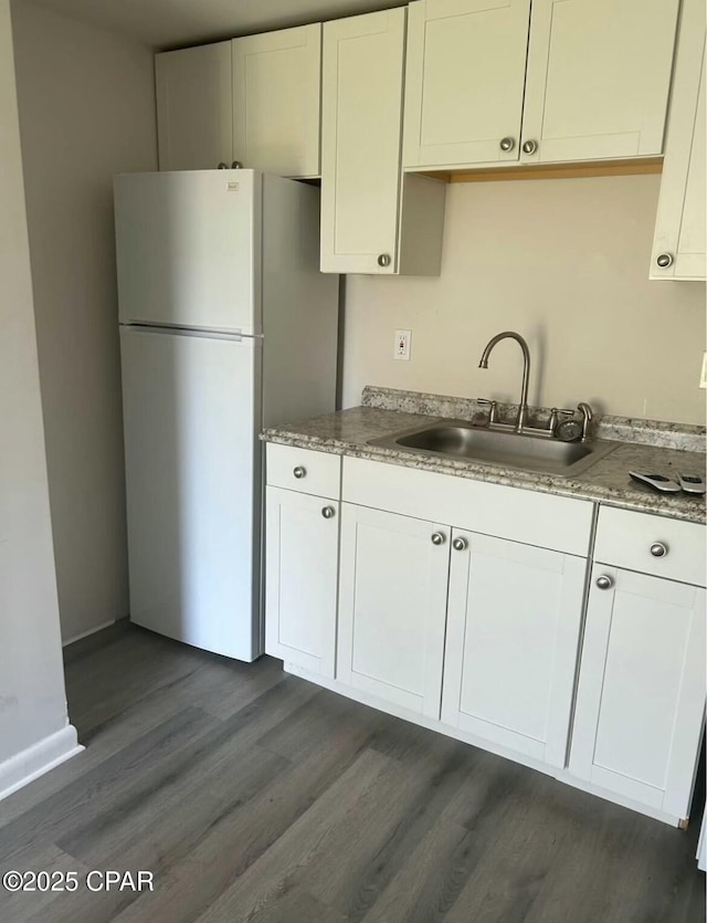 kitchen with light stone counters, a sink, dark wood-type flooring, freestanding refrigerator, and white cabinetry