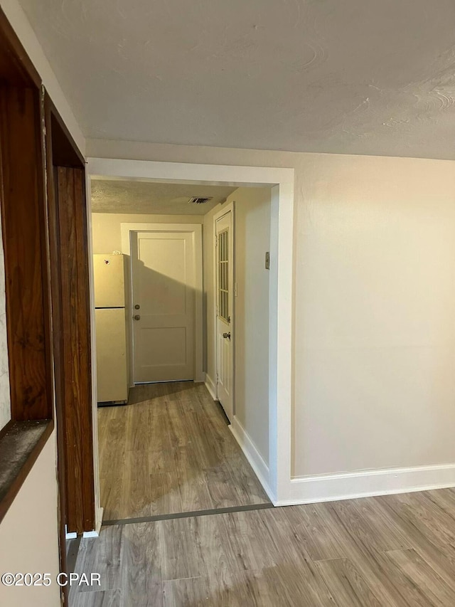 hall featuring baseboards, wood finished floors, and visible vents
