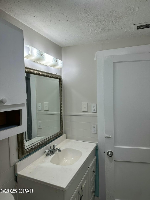 bathroom with a wainscoted wall, a textured ceiling, tile walls, visible vents, and vanity