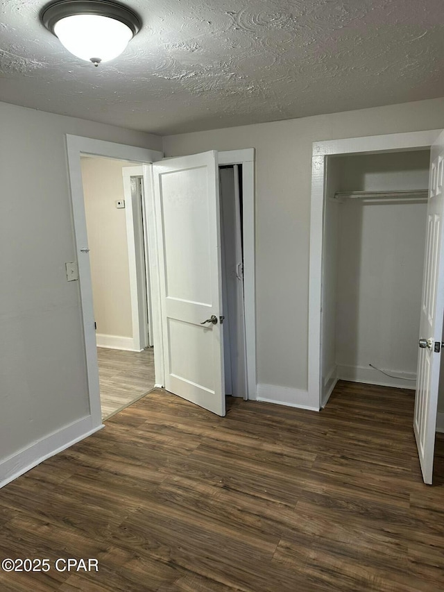 unfurnished bedroom with dark wood-type flooring, a textured ceiling, baseboards, and multiple closets