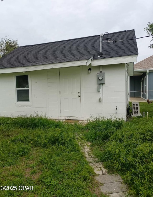 back of property with roof with shingles and concrete block siding