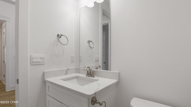 half bathroom with vanity, wood finished floors, and toilet