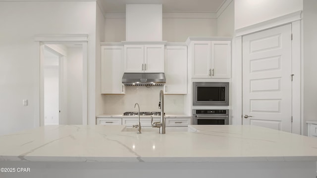 kitchen featuring light stone countertops, a center island with sink, under cabinet range hood, white cabinets, and stainless steel appliances