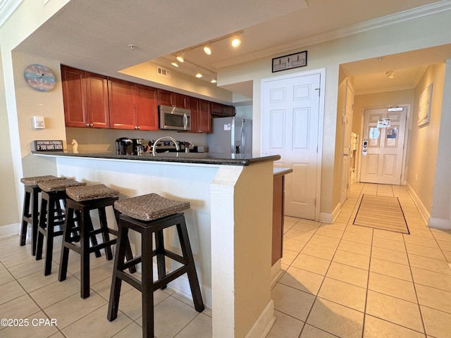 kitchen with stainless steel appliances, ornamental molding, light tile patterned floors, and a peninsula