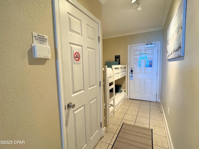corridor with light tile patterned floors, baseboards, ornamental molding, and a textured wall