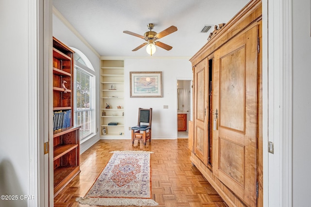 sitting room with visible vents, crown molding, ceiling fan, and built in shelves