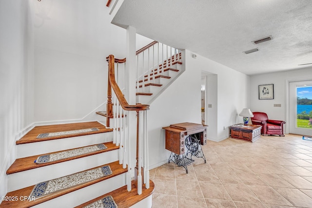 stairway with baseboards, a textured ceiling, visible vents, and tile patterned floors