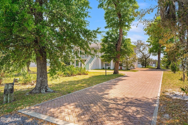 view of property's community with a lawn, decorative driveway, and stairway