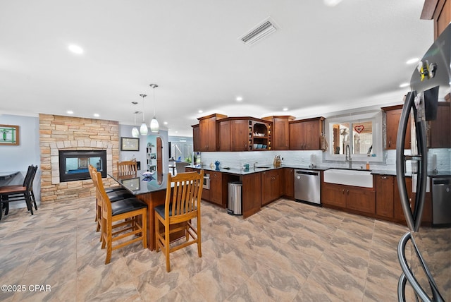 kitchen with stainless steel dishwasher, freestanding refrigerator, decorative backsplash, a fireplace, and a sink