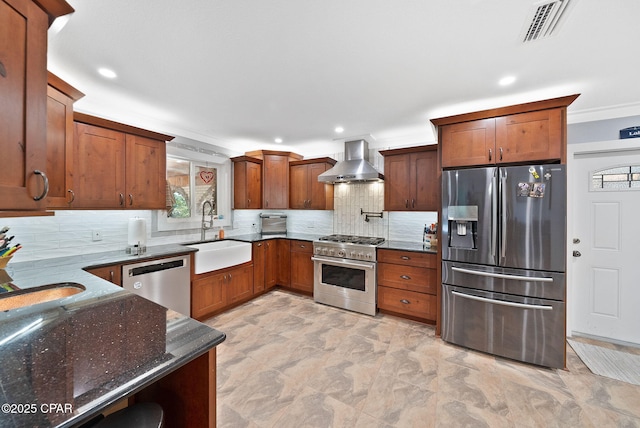 kitchen with wall chimney range hood, dark stone countertops, a sink, visible vents, and stainless steel appliances