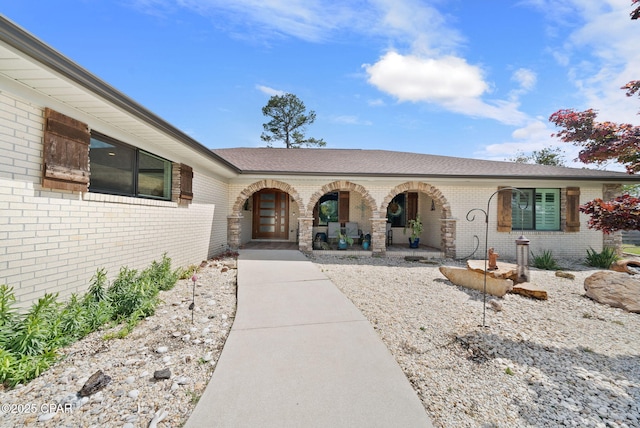 entrance to property featuring covered porch, a shingled roof, and brick siding