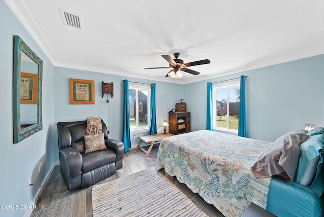 bedroom featuring baseboards, visible vents, a ceiling fan, wood finished floors, and ornamental molding