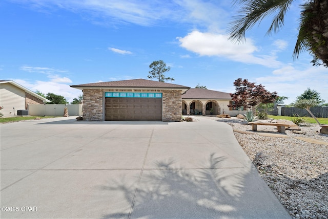 prairie-style home featuring fence, central air condition unit, a garage, driveway, and stone siding