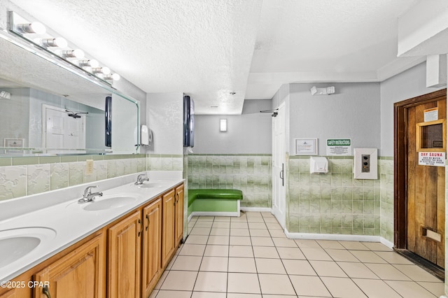 full bathroom featuring a sink, a wainscoted wall, double vanity, and a textured ceiling
