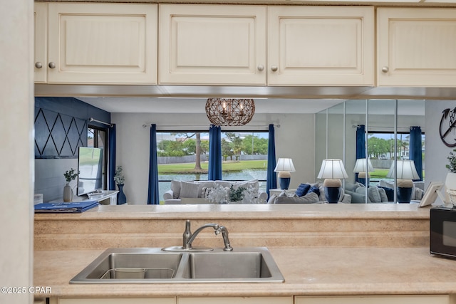 kitchen featuring a sink, cream cabinetry, a healthy amount of sunlight, black microwave, and light countertops