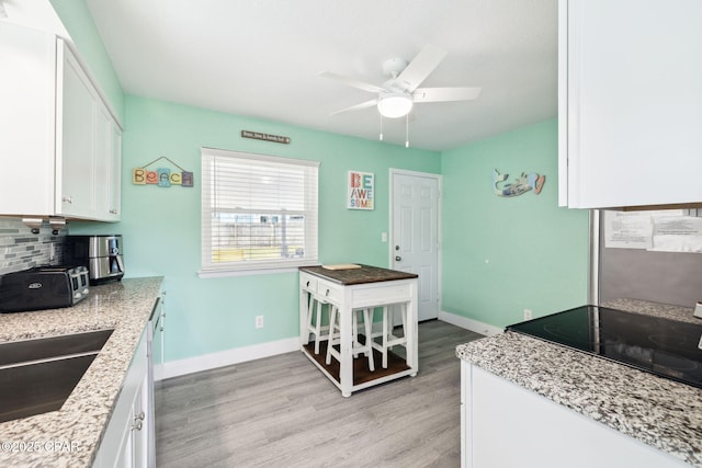 kitchen with white cabinets, ceiling fan, baseboards, light wood-type flooring, and backsplash