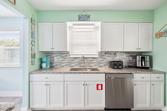 kitchen featuring stainless steel dishwasher, a sink, white cabinetry, and tasteful backsplash