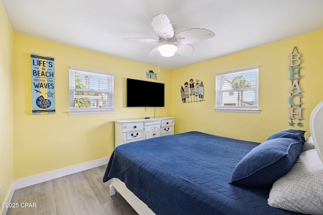 bedroom featuring baseboards, ceiling fan, wood finished floors, and multiple windows