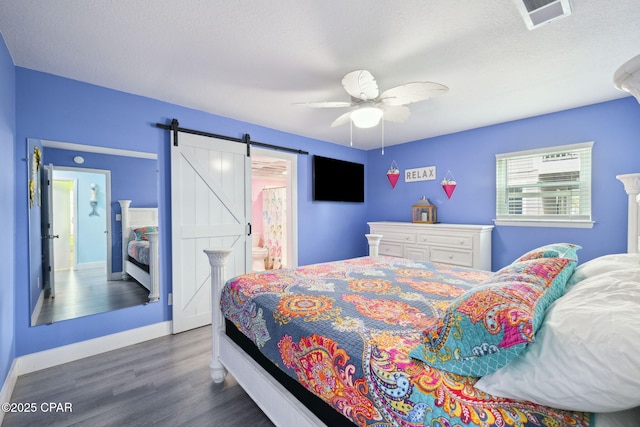 bedroom with ceiling fan, visible vents, a barn door, wood finished floors, and baseboards