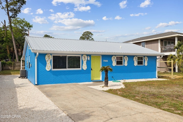 view of front of house featuring fence, brick siding, metal roof, central air condition unit, and driveway