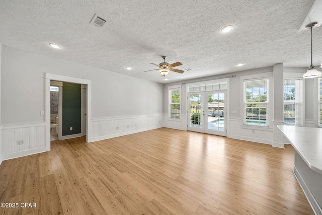 unfurnished living room featuring a ceiling fan, a textured ceiling, visible vents, wainscoting, and light wood-style floors