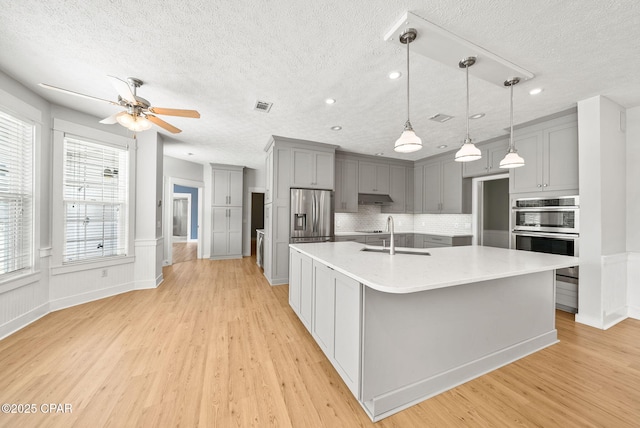 kitchen featuring light wood-style flooring, gray cabinetry, a textured ceiling, visible vents, and appliances with stainless steel finishes