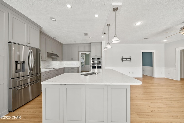 kitchen with a sink, stainless steel appliances, a textured ceiling, gray cabinetry, and light wood-style floors