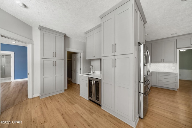 kitchen featuring a sink, stainless steel refrigerator with ice dispenser, gray cabinets, and beverage cooler