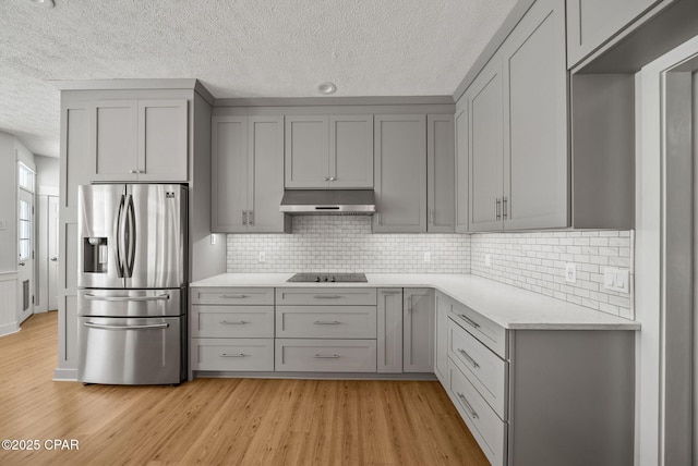 kitchen with gray cabinets, a textured ceiling, under cabinet range hood, black electric cooktop, and stainless steel fridge with ice dispenser