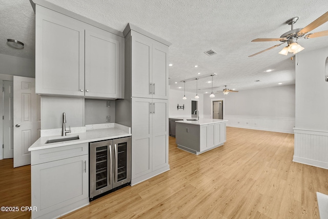 kitchen featuring a sink, wine cooler, a textured ceiling, ceiling fan, and light wood-style flooring
