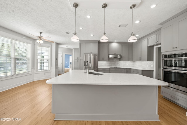 kitchen with a textured ceiling, a sink, light wood-style floors, appliances with stainless steel finishes, and gray cabinets