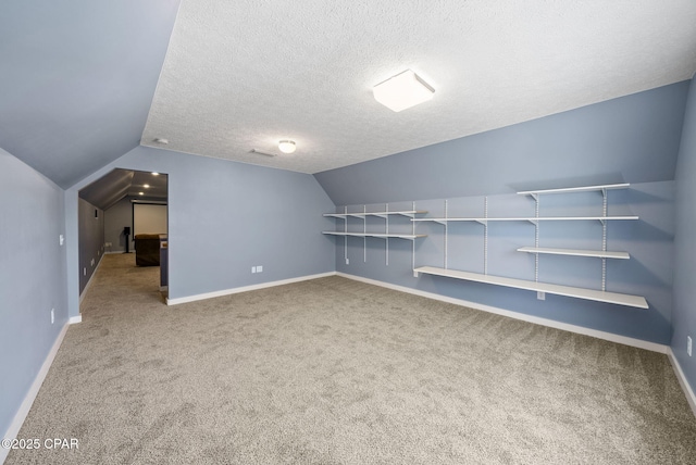 additional living space featuring a textured ceiling, vaulted ceiling, baseboards, and carpet floors