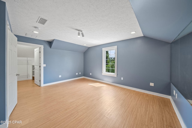 additional living space with vaulted ceiling, light wood-style flooring, baseboards, and visible vents