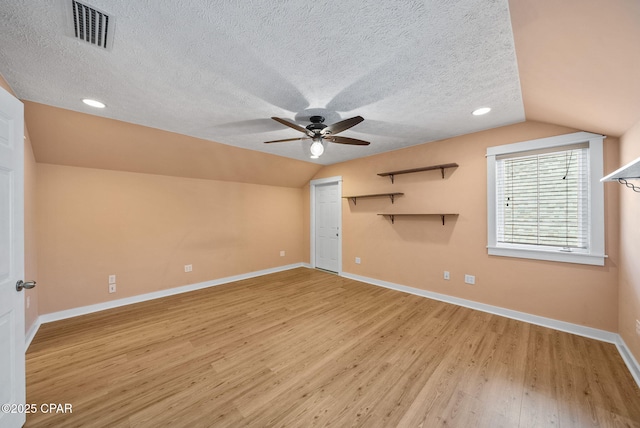 interior space featuring light wood finished floors, a ceiling fan, a textured ceiling, visible vents, and vaulted ceiling