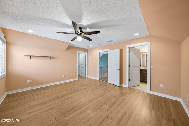 unfurnished bedroom featuring a textured ceiling, visible vents, baseboards, ensuite bathroom, and light wood-style floors