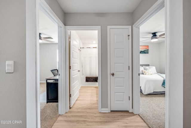 hallway with baseboards, light colored carpet, and light wood-style flooring