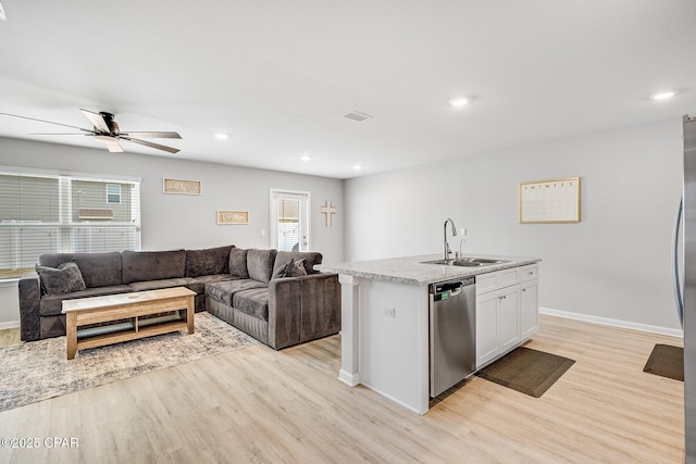 kitchen with stainless steel dishwasher, a sink, light wood-style floors, light countertops, and open floor plan