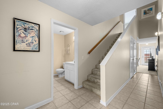 stairs featuring a textured ceiling, tile patterned floors, and baseboards