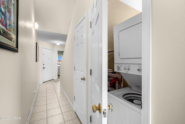 clothes washing area featuring light tile patterned floors, stacked washer and clothes dryer, laundry area, and baseboards