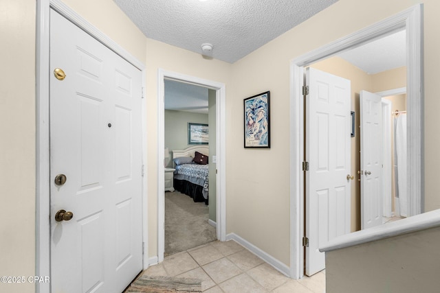 hall with baseboards, light tile patterned floors, a textured ceiling, and light colored carpet