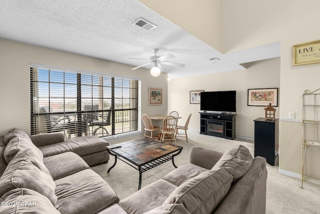 living room with a ceiling fan, visible vents, light colored carpet, and a textured ceiling